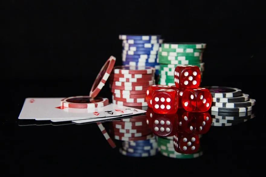 Red dice, stacked casino chips, and playing cards arranged on a dark reflective surface