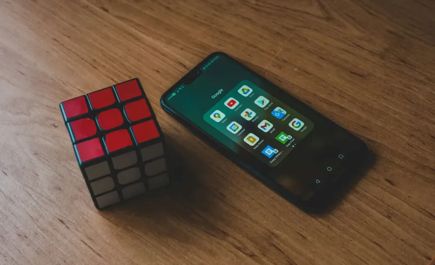 Smartphone showing Google app icons next to a Rubiks cube on wood