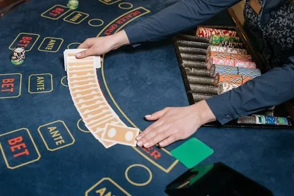 Dealer fanning playing cards over a blue ante and bet layout with chips