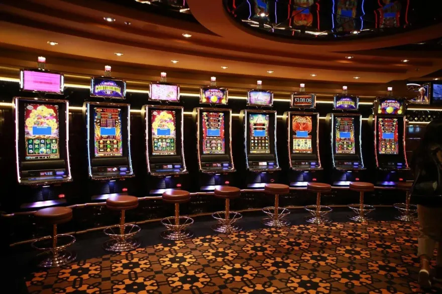 Row of illuminated slot machines with stools on a casino floor